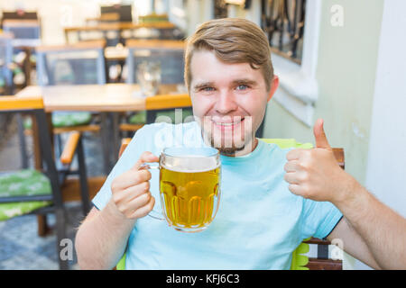Gioioso uomo sorridente tenendo un grande boccale di birra e che mostra i pollici fino all'aperto Foto Stock