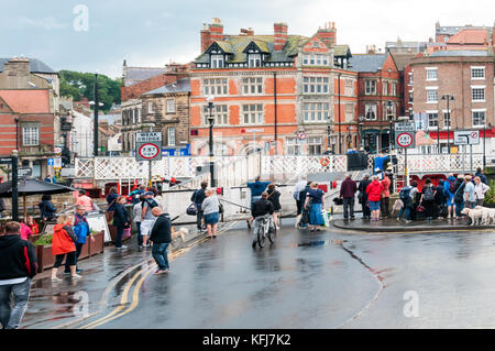 Pedoni in attesa per il ponte girevole attraverso il porto di Whitby per aprire. Foto Stock