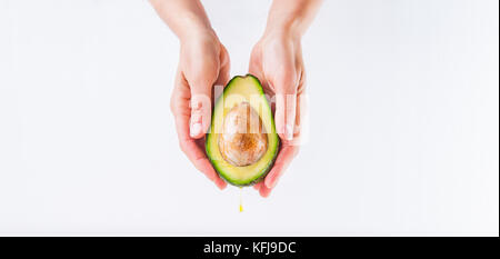 Fresh avocado con olio cadere in mani femminili sullo sfondo bianco isolato. sani e naturali di bellezza concetto. vista frontale. spazio per il testo. wide photo. Foto Stock