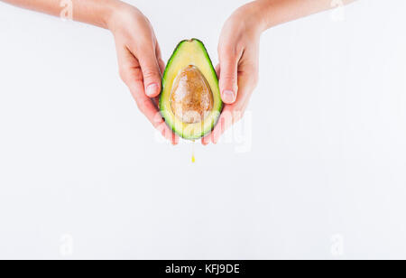 Fresh avocado con olio cadere in mani femminili sullo sfondo bianco isolato. sani e naturali di bellezza concetto. vista frontale. spazio per il testo Foto Stock