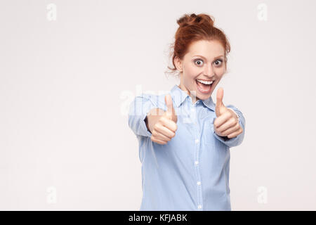 Felice allegro redhead donna che mostra un pollice alzato e il sorriso toothy. isolato studio shot su sfondo grigio Foto Stock