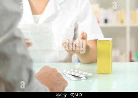 Close up di un farmacista la lettura di foglietto illustrativo di un farmaco ad un paziente in una farmacia indoor Foto Stock