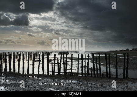 Pioggia nuvole si muovono in su un mersea Island Beach a bassa marea, bradwell centrale nucleare e bradwell wind farm all'orizzonte Foto Stock