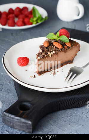 Fetta di Cheesecake al cioccolato decorata con mandorle, lamponi e foglia di menta su sfondo scuro. verticale, il fuoco selettivo Foto Stock