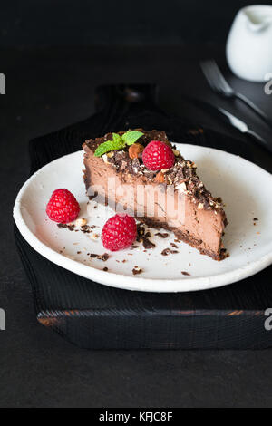 Fetta di Cheesecake al cioccolato decorata con mandorle, lamponi e foglia di menta su sfondo scuro. verticale, il fuoco selettivo Foto Stock