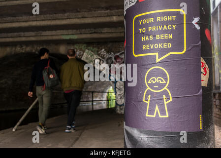 Street Art poster appeso su colonna nei pressi di un tunnel da artista subdude con uomo stilizzato e fumetti con slogan 'il tuo diritto alla privacy è stato revocato'. Foto Stock
