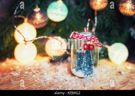 Due piccoli arte alberi di Natale in un vasetto di vetro n anteriore di un ramo di Natale decorato con palle di Natale Foto Stock