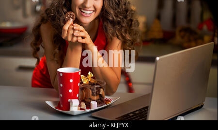 Felice giovane casalinga con spuntini di natale utilizzando laptop in cucina Foto Stock