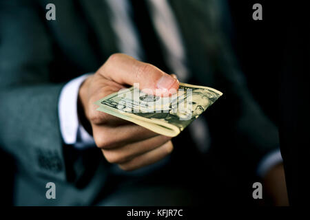 Un giovane uomo caucasico in un elegante abito grigio seduto nel sedile posteriore di una vettura offre un batuffolo di fatture del dollaro nella parte anteriore Foto Stock