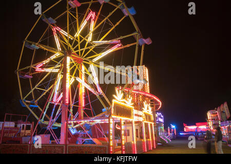 Il viaggio luna park di notte con luci luminose in fiera con illuminato grande ruota panoramica Ferris REGNO UNITO Foto Stock