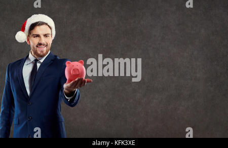 Un imprenditore con la barba in una santa claus hat detiene un piggy ba Foto Stock