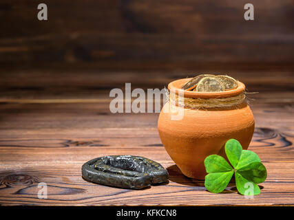 Il giorno di San Patrizio concetto con pentola piena di monete d'oro, a ferro di cavallo e shamrock su vintage sfondo di legno, close up Foto Stock