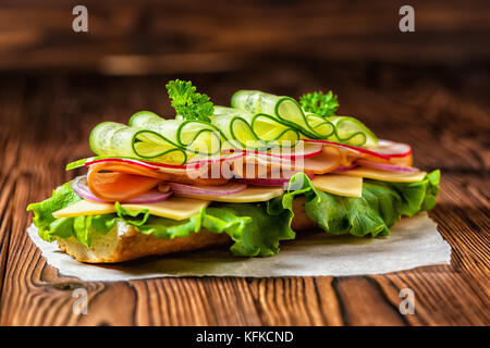 Bella sandwich con prosciutto e formaggio, pancetta, Rafano, lattuga, cetrioli e cipolle sul legno scuro sfondo, close up Foto Stock