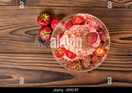 Top down di dessert Fragola Rosa gelato alla vaniglia scoop con spruzzata di Cioccolato e fragole fresche in vaso su sfondo di legno Foto Stock