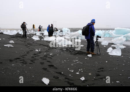 Fotografi in tour fotografico con fotocamere e cavalletti in piedi e fotografando iceberg lavati su una spiaggia di diamanti di sabbia nera a Jokulsarlon Islanda Foto Stock