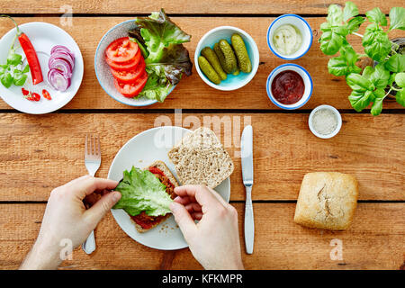 Facendo un panino vegano freschi ingredienti organici mano insalata di aggiunta Foto Stock