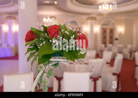 Rose rosse centrotavola a un ricevimento di matrimonio. Visualizzazione decorativa di un allestimento floreale in un grande locale Foto Stock