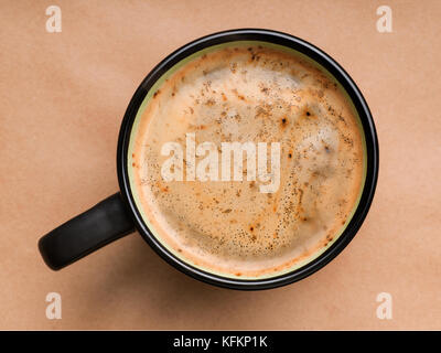 La schiuma del caffè in tazza nera vista dall'alto. su marrone craft sfondo della carta Foto Stock