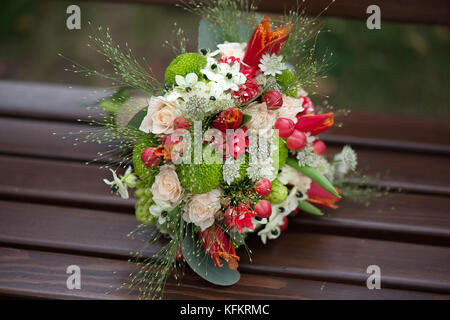 Fiori, foglie e bacche di un giro in un gusto floreale nuziale disposizione in appoggio su una panca in legno con sfondo sfocato Foto Stock