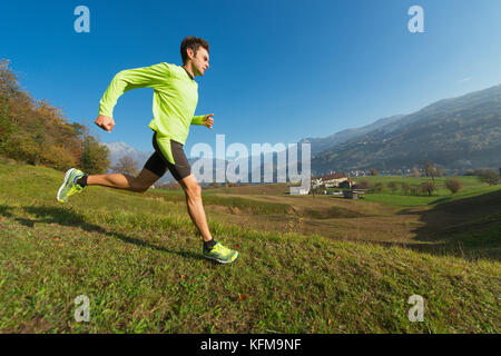 Atleta corre in discesa nel prato in una valle delle Alpi italiane. Foto Stock