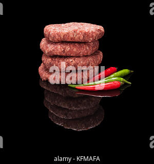 Pila di greggio polpette di carne di manzo con peperoncino isolato nero su sfondo lucido con una vera riflessione. vista laterale Foto Stock