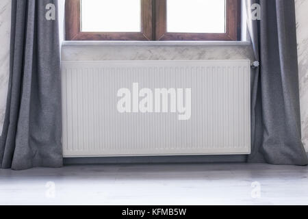 Il radiatore di riscaldamento sotto la finestra con un telaio in legno e le tende. Foto Stock