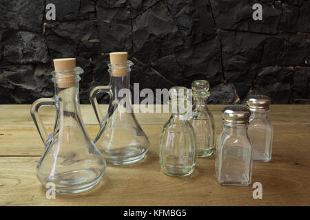 Olio d'oliva, aceto di bottiglie di vetro, il sale e il pepe impostato sul tavolo di legno, nero contro il muro di pietra Foto Stock