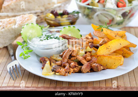 Carne di maiale greca gyros su una piastra bianca, servita con tzatziki e patate fritte, pitabread, insalata e olive Foto Stock