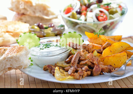 Carne di maiale greca gyros su una piastra bianca, servita con tzatziki e patate fritte, pitabread, insalata e olive Foto Stock