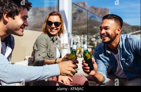 Gruppo di amici birre di tostatura ad una festa sul tetto. Giovani uomini e donne appendere fuori a parte sul tetto e godersi un drink. Foto Stock