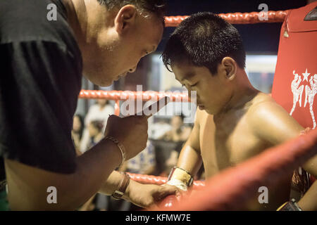 Giovane boxe tailandese seduto nel conner del ring, consigliato dal suo allenatore, tra le partite, Bangkok, Thailandia Foto Stock