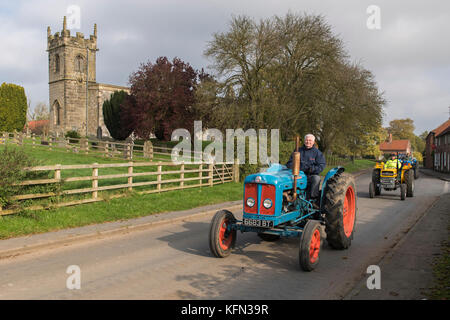 Uomo alla guida di vecchio blu vintage trattore attraverso il villaggio di Bugthorpe su Wolds Gruppo Vintage Road Run, annualmente un evento di beneficenza - Yorkshire, Inghilterra, Regno Unito. Foto Stock