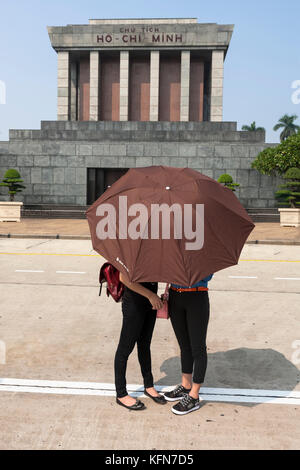 Due giovani studenti si nascondono dietro un ombrello di fronte all'imponente Mausoleo di ho Chi Minh, Hùng Vương, Điện Biên, Ba Đình, Hà Nội, Viet Nam Foto Stock