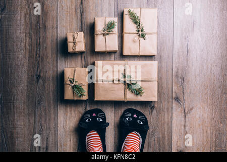 Piedi con il caldo inverno calze e cat pantofole in piedi di fronte a Doni di natale. vista dall'alto. Foto Stock