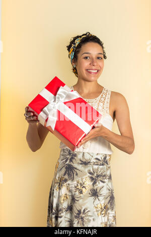 Nero donna con capelli corti è in possesso di un regalo di Natale. casella rossa con pizzo bianco. indossa modellato e abiti colorati. Foto Stock