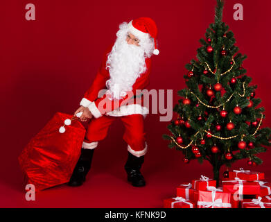 Santa tirando doni sacco e in piedi vicino all albero di natale Foto Stock