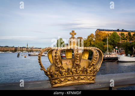 Royal Crown sul ponte a isola di Skeppsholmen e la città con il palazzo reale dietro, Stoccolma, Svezia Foto Stock