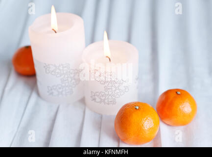 Due candele festosa, tangerini su una tovaglia bianca Foto Stock