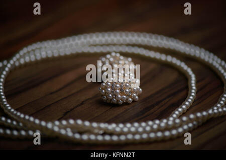 Elegante collana di perle e grandi Abbellito Orecchini posizionato al buio su un tavolo di legno Foto Stock