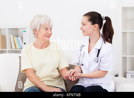 Ritratto di giovane medico tenendo la mano del paziente maturo Foto Stock