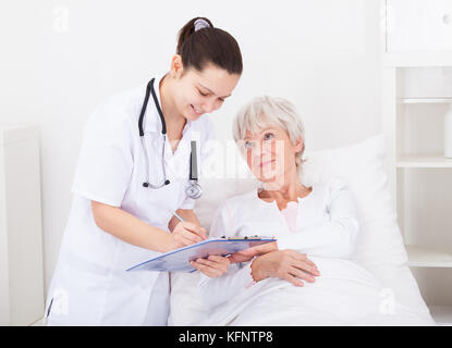 Senior paziente femmina guardando medico iscritto negli appunti Foto Stock