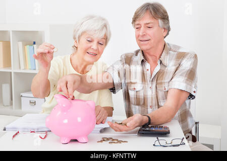 Ritratto di sorridente coppia senior il calcolo di monete in rosa piggybank Foto Stock