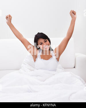 Giovane donna felice stretching le braccia sul letto Foto Stock