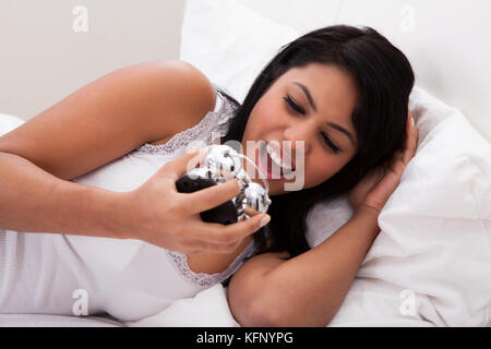 Overslept donna sdraiata sul letto guardando sveglia Foto Stock