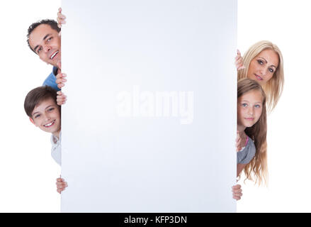 Ritratto di famiglia con due bambini di sbirciare dietro la scheda in bianco su sfondo bianco Foto Stock