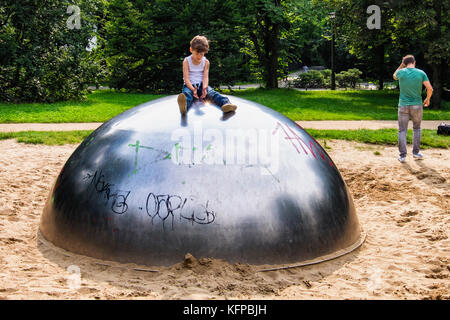 Berlin volkspark priedrichshain, parco pubblico. giovane ragazzo cattura la luce del sole in un'area gioco per i bambini con buca di sabbia e lucido semi-sfera sfera Foto Stock