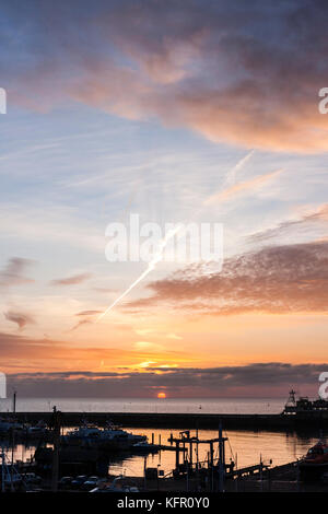 Sun salito sopra l'orizzonte oltre la Manica. Il sole è una sfera rossa appena circa per agganciare un strato di nube spessa sopra. Orange sky. Ramsgate Harbour in primo piano. Foto Stock