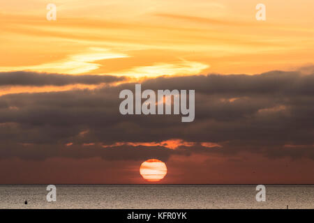 Sun salito sopra l'orizzonte oltre la Manica. Il sole è una sfera rossa appena circa per agganciare un strato di nube spessa sopra. Orange sky. Visto da di Ramsgate nel Kent. Foto Stock