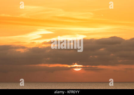 Il sorgere del sole sopra il canale inglese. Sun sopra l'orizzonte parzialmente nascosti dallo strato di nubi. Orange sky. Visto da di Ramsgate nel Kent. Foto Stock