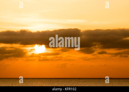 Il sorgere del sole sopra il canale inglese. Sun sopra l'orizzonte parzialmente nascosti dallo strato di nubi. Orange sky. Visto da di Ramsgate nel Kent. Foto Stock